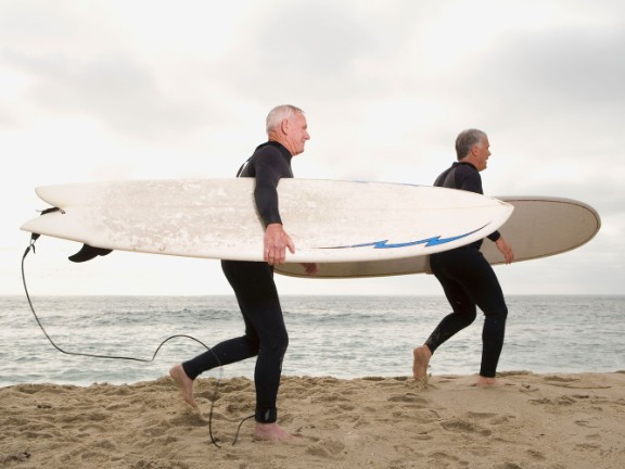 Senior surfers on the beach carrying surfboards over their heads.