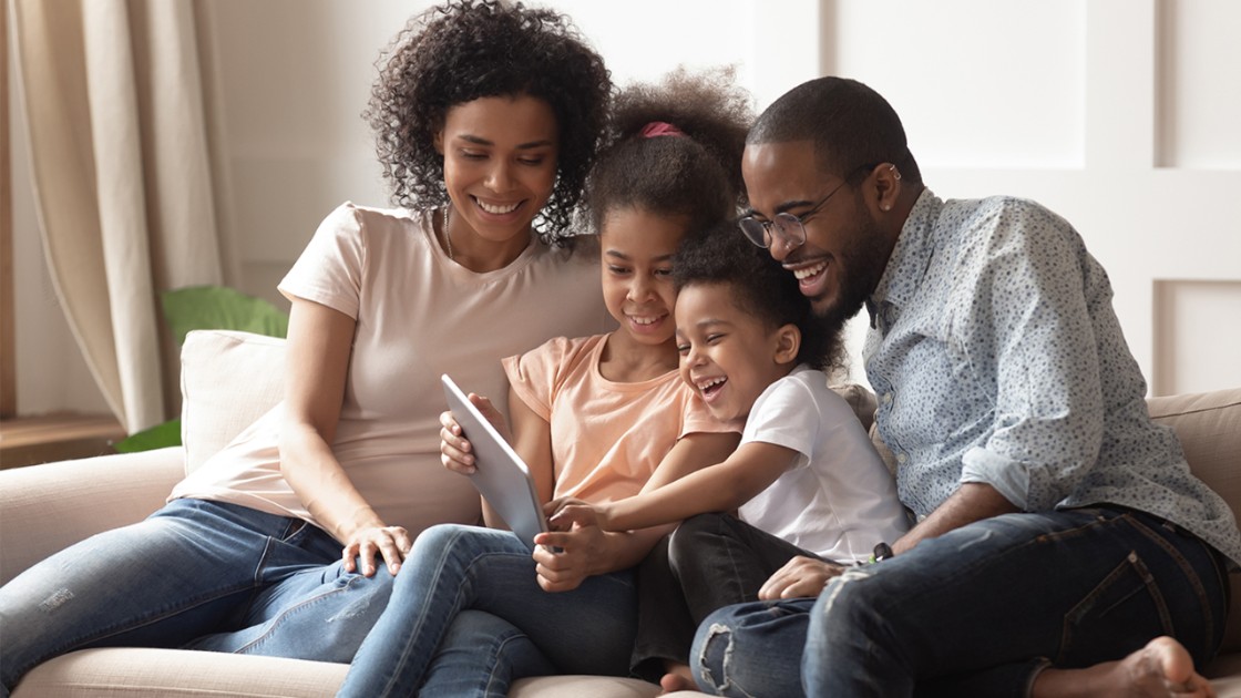 A couple with two young children enjoy time together on the couch with a tablet 