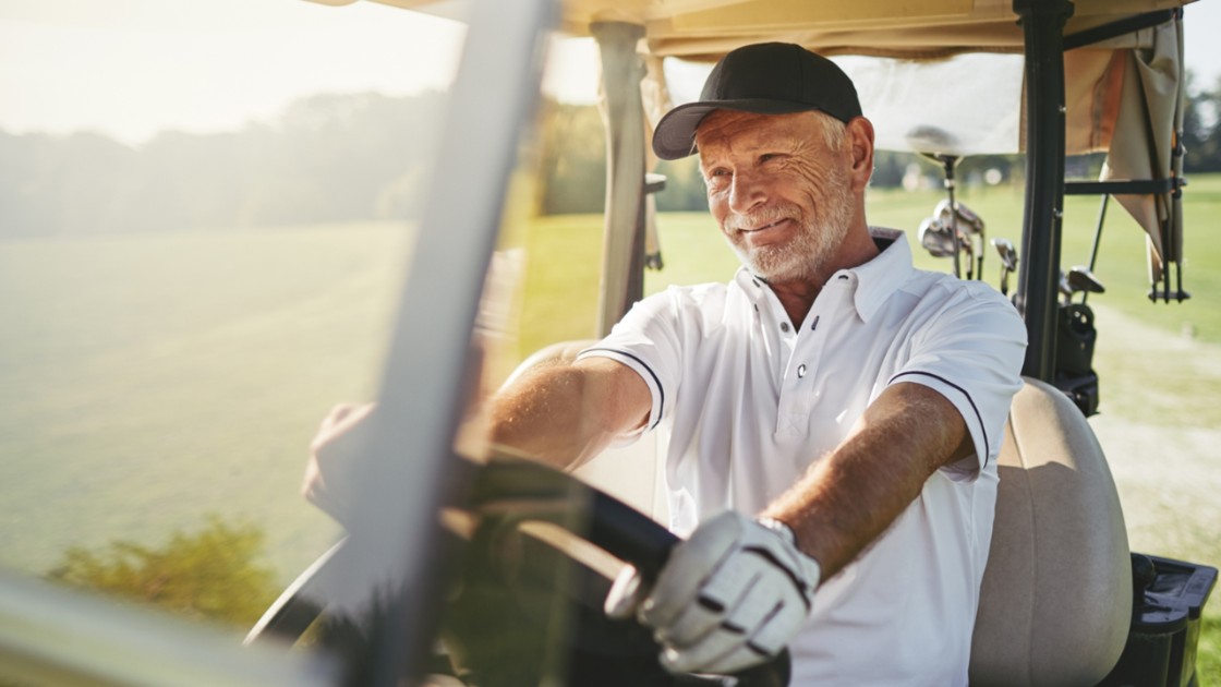 Senior man smiling as he drives a golf cart along a golf course