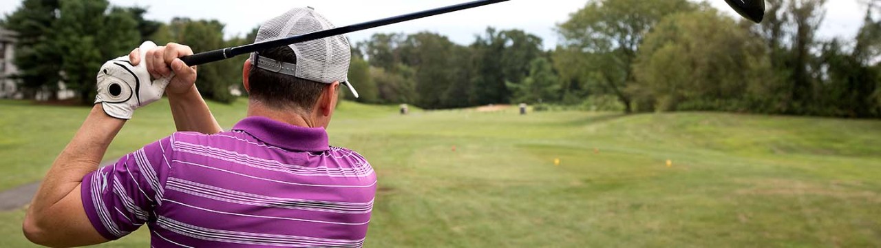 Man in a purple polo shirt takes a swing on the golf course during an overcast day