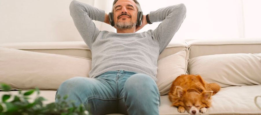Middle-aged man lying on couch with headphones and smiling