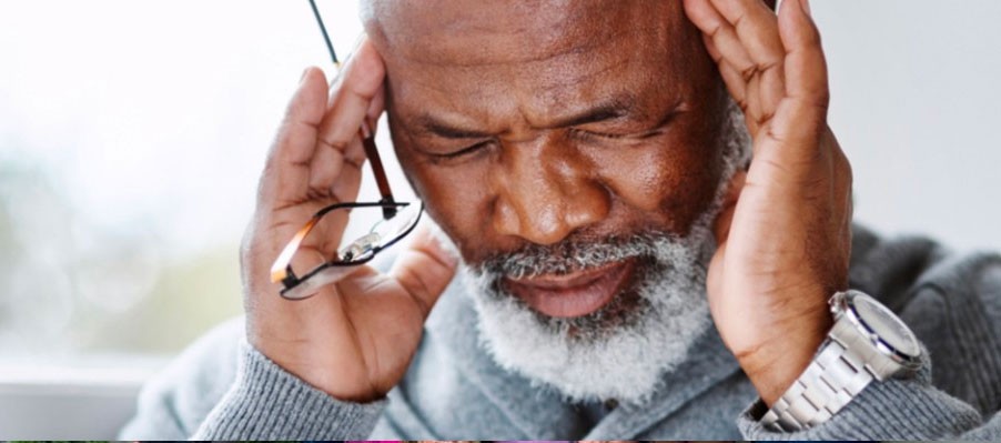 Senior male holding his temples and squinting and looking down.