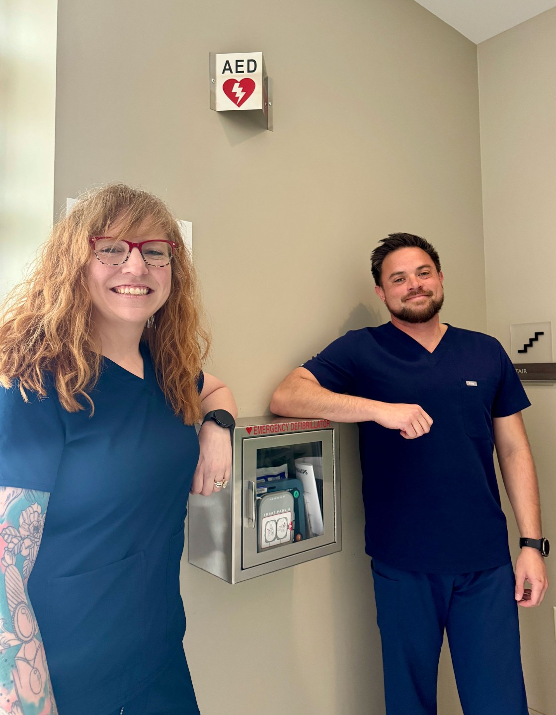 Jessica Bower, the Senior Director of Cardiovascular Services for Dignity Health Central Coast, and Greg Larsen, AED Program Coordinator at French Hospital, pose with a wall-mounted AED unit. French Hospital has received a grant that will help distribute 20 AEDs throughout the City of San Luis Obispo.