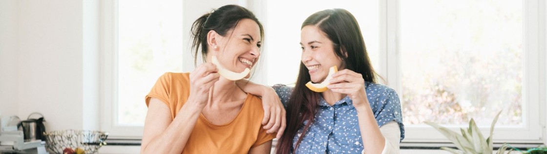 Mother and daughter smiling eating veggies.