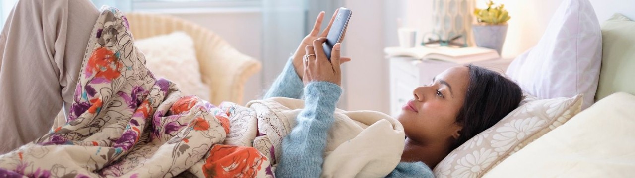 Teenage girl laying on bed looking at her phone.