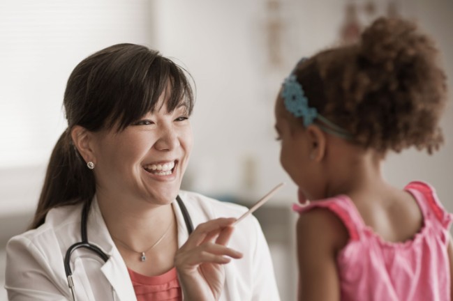 Doctor checking pediatric patient's throat and laughing